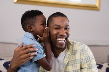 Boy whispering father on sofa at home - Powered by Adobe