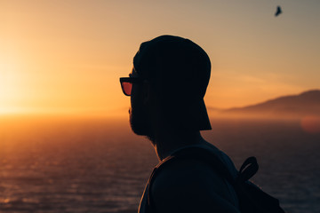 A young man watches the sunset over the Pacific Ocean