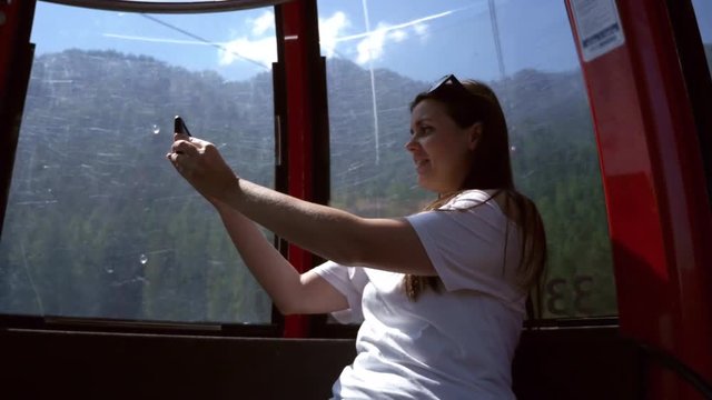 Woman happy in cableway in mountains enjoying vacation in summer taking selfie