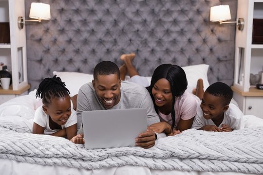 Smiling family using laptop while lying together on bed