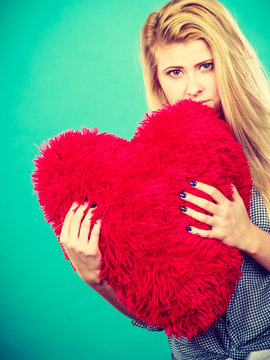 Sad woman holding red pillow in heart shape