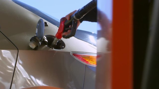 Tracking shot of hands of gas station attendant inserting fuel nozzle into opened car tank 