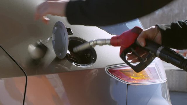 Tilt up shot in slow motion of male hands putting fuel nozzle into opened car tank 