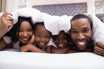 Portrait of happy family lying together under blanket on bed