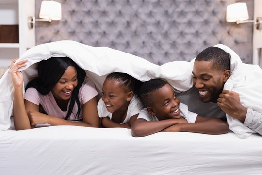 Happy family lying together under blanket on bed