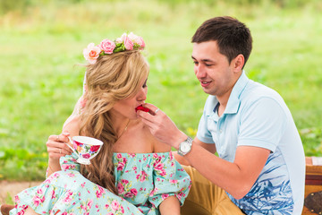 Obraz premium Handsome man is feeding his beautiful woman with a delicious donut in picnic on nature