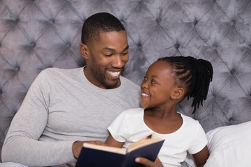 Happy man with daughter reading book on bed