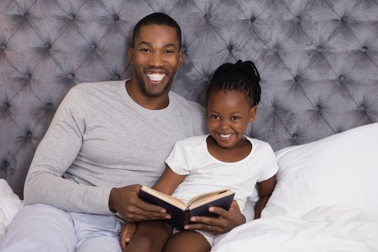 Portrait of smiling man with daughter reading book on bed