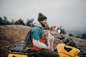 Young bearded man and his dog sitting on the quadro motorcycle in nature