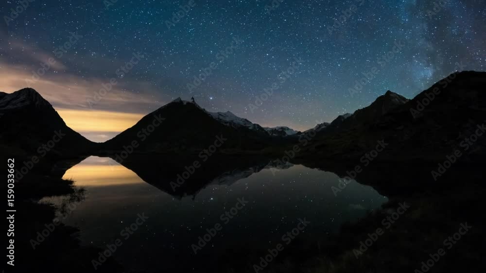 Wall mural the apparent rotation of the milky way and the starry sky beyond snowcapped mountain ridge, reflecte