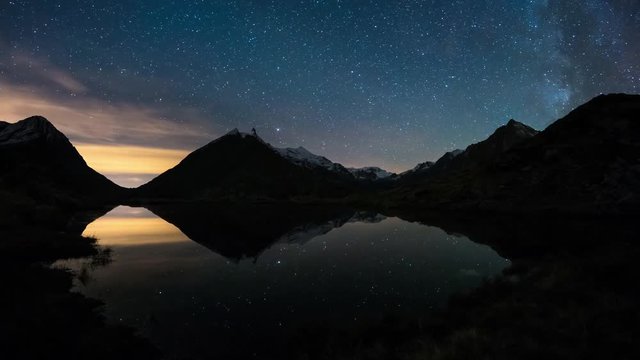 The apparent rotation of the Milky Way and the starry sky beyond snowcapped mountain ridge, reflected on idyllic apine lake. Orion Constellation coming from left at the end. Time Lapse 4k video. 