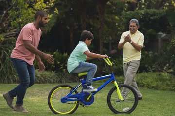 Fototapeta premium Father and grandfather motivating boy while riding bicycle