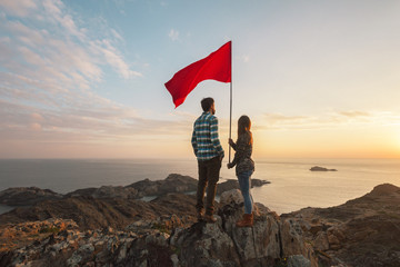 Young couple with red flag in a cliff of a sunrise