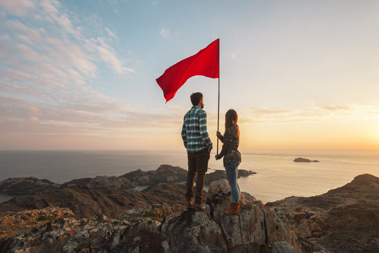 Young couple with red flag in a cliff of a sunrise