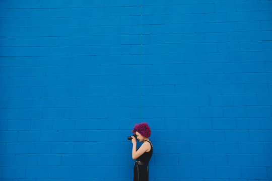 Woman against blue brick wall taking a photograph