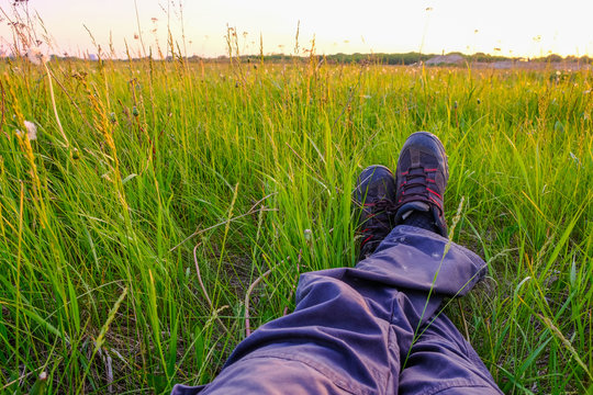Male feet on green grass at sunset