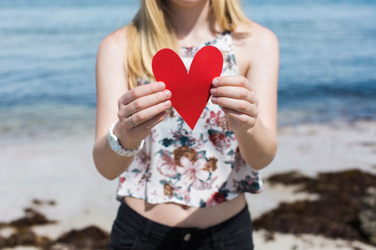 Mid section of a woman holding a red heart on the beach