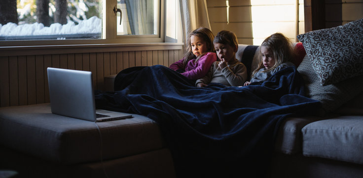 Three kids watching laptop inside during winter day
