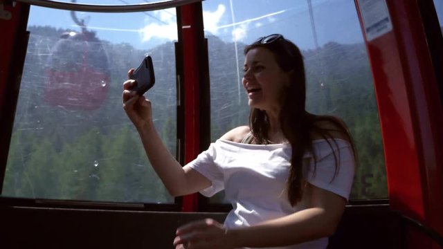 Woman in cableway in mountains making video phone call showing to friends the view