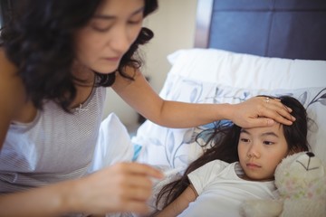 Mother checking body temperature of sick daughter in bed room