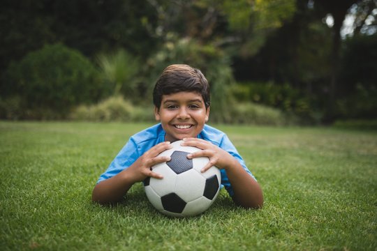 Portrait of smiling boy with soccer ball lying at park