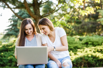 Two best friends in park,smiling and working on laptop