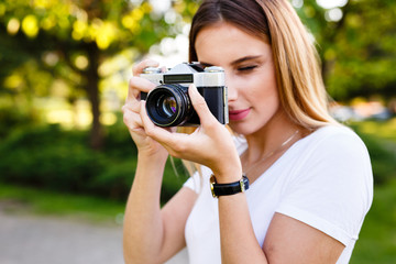 Cute girl on sunny day in park taking photos with analog camera