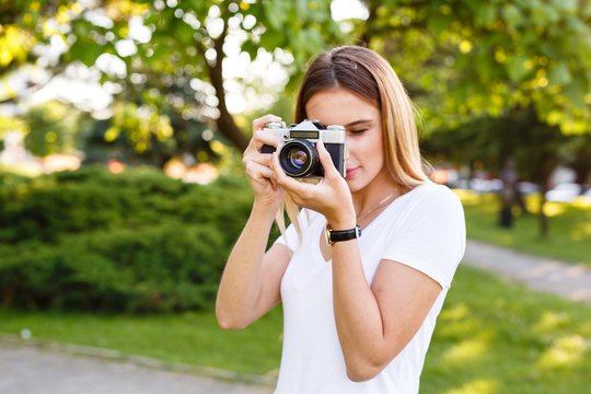 Cute girl on sunny day in park taking photos with analog camera
