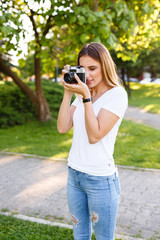 Cute girl on sunny day in park taking photos with analog camera