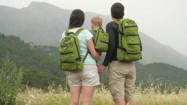 A Young Family Of Travelers With A Baby Looking Back At The Mountains. Everyone Has The Same Green Backpacks.