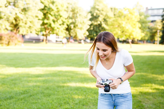 Cute girl in park smiling while taking photographs with her camera