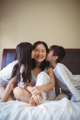 Siblings kissing mother on cheeks in the bed room