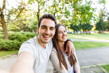 Obraz premium Cute and happy couple enjoying in park and taking selfie