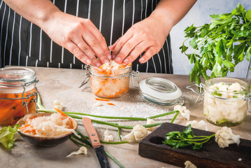 Concept of fermented meal. Home canned food and billets. Vegan food. Vegetables. Person (woman) cooking sauerkraut. Cans with conservation, broccoli, carrots, greens, onions.