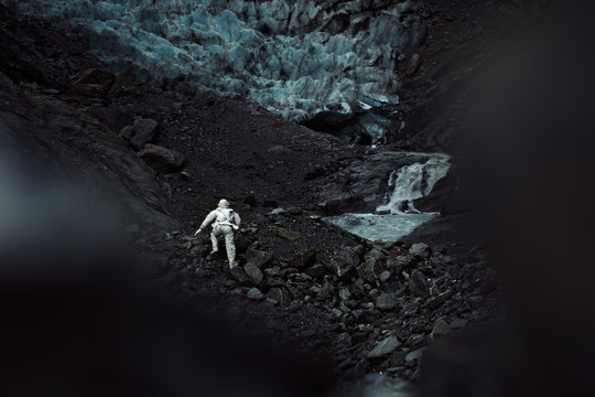 A lone astronaut climbs the side of a rocky and icy mountain