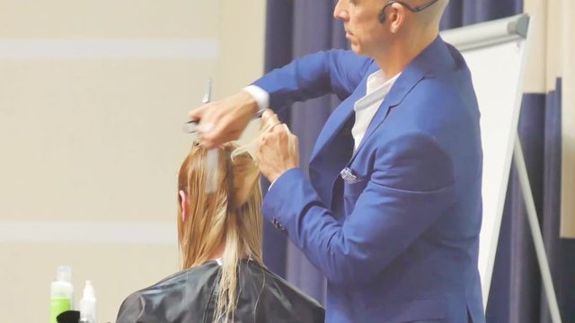 Stylist man cuts hair blonde Italian in a hairdressing salon