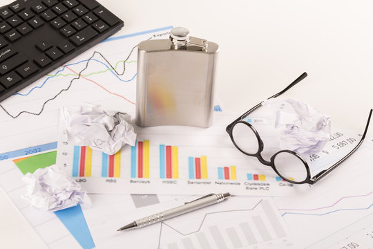 Desk with graphs, keyboard, glasses, pen, shredded papers and bottle of alcohol