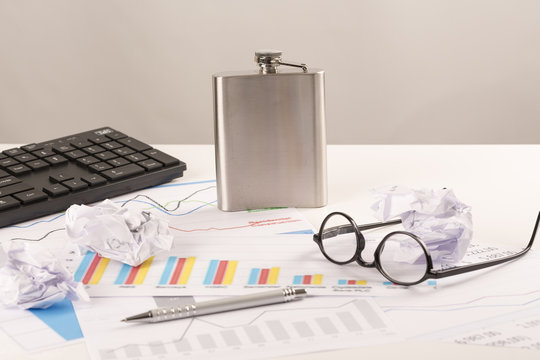 Desk with graphs, keyboard, glasses, pen, shredded papers and bottle of alcohol