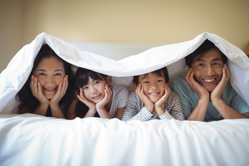 Family relaxing together under a blanket in bedroom