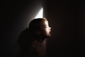Profile of young boy in small batch of light in dark room
