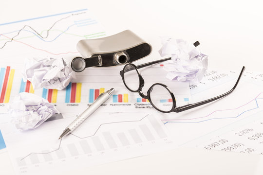 Desk with graphs, keyboard, glasses, pen, shredded papers and bottle of alcohol