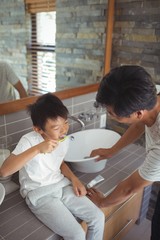 Son brushing his teeth with father in bathroom