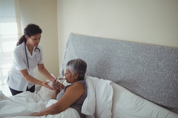 Obraz premium Female doctor giving sick senior woman a glass of water on bed