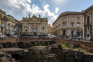 Fototapeta na wymiar Ruins of the Roman Amphitheater at the Stesicoro Square with San Biagio Church on background - Catania, Sicily, Italy