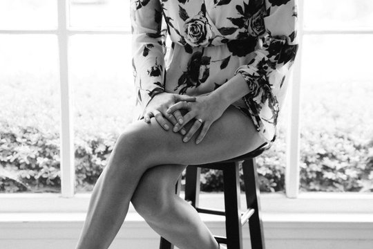 young female crossing legs while sitting on stool in front of window