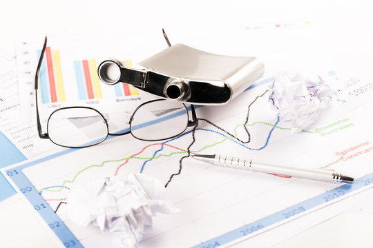 Desk with graphs, keyboard, glasses, pen, shredded papers and bottle of alcohol