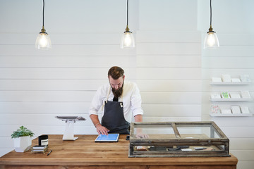 Small business owner working on digital tablet in artisan retail shop