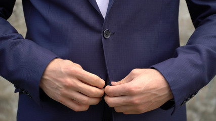 The man fastens buttons on his jacket close up.