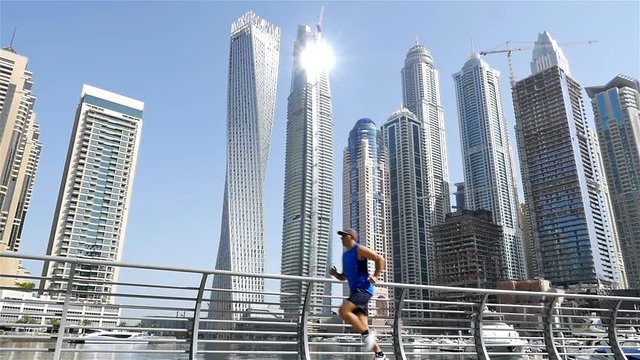 Low angle view of athletic fitness man running jogging in Dubai Marina in the morning, slow motion