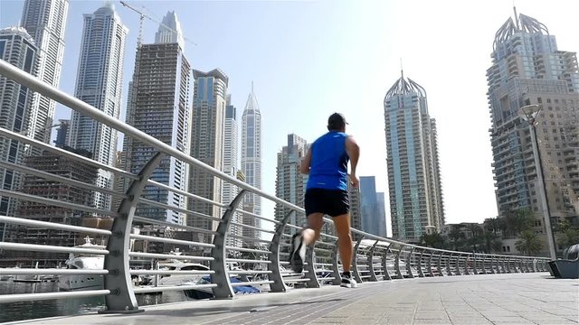 Low angle view of athletic fitness man running jogging in Dubai Marina in the morning, slow motion
